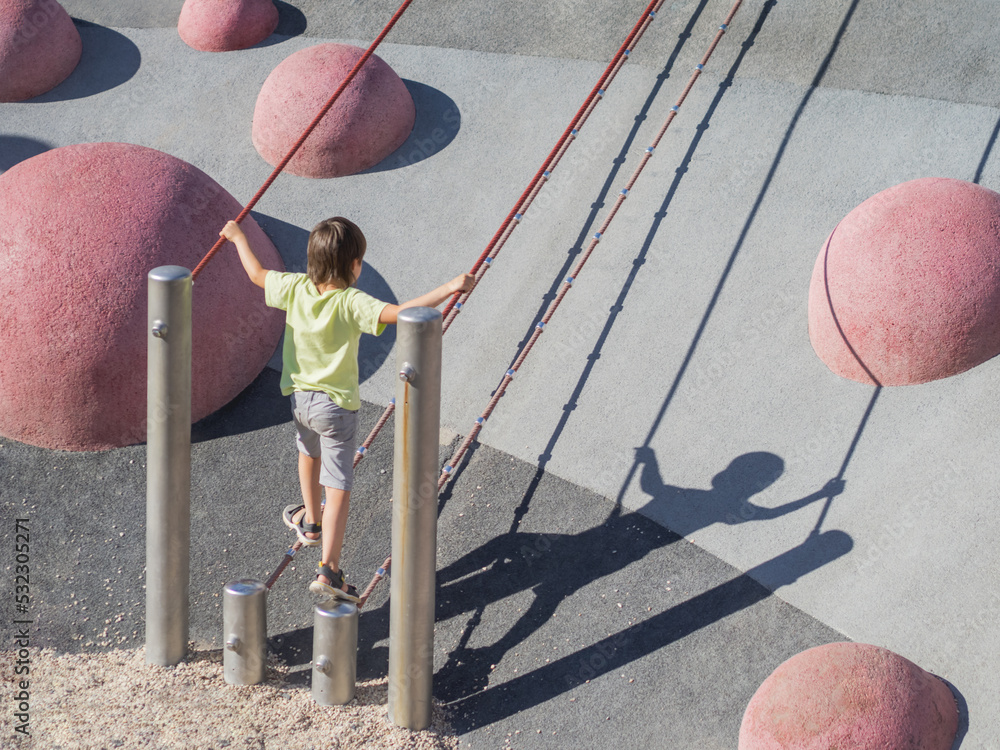 Boy climbes up a concrete slope of modern children's sports and playground. Kid overcomes fear and learn new things. Active leisure outdoors. Sporty lifestyle.